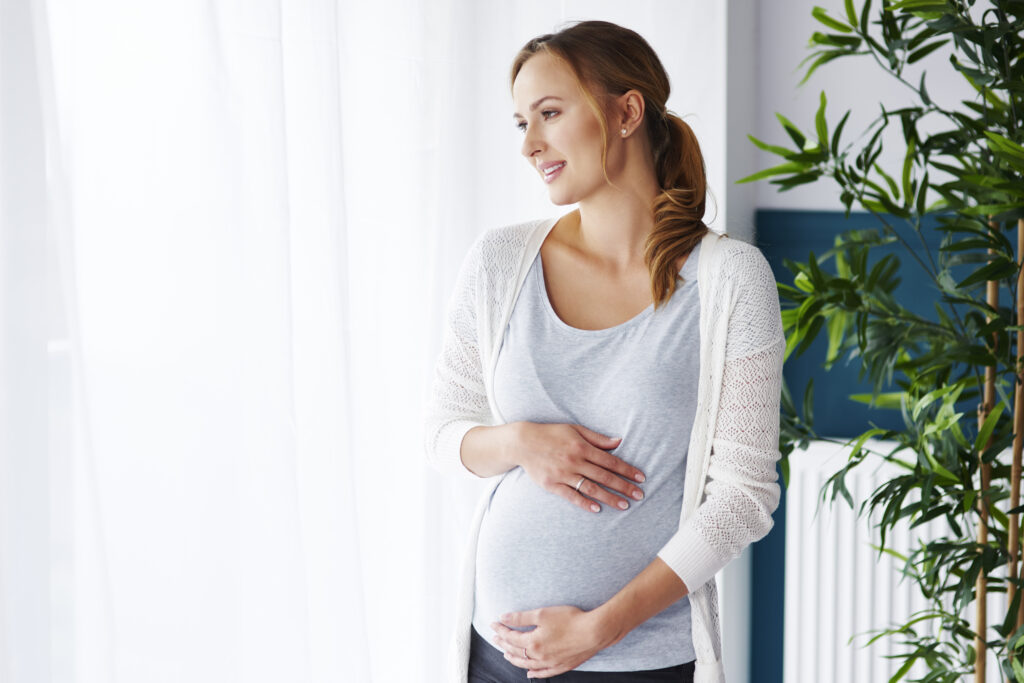 cheerful pregnant woman looking through window